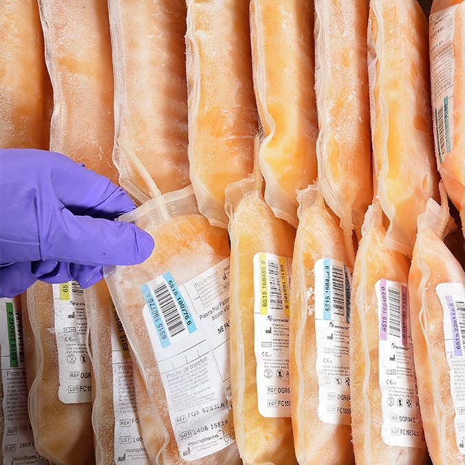 Two rows of plasma bags lined up one below the other. A gloved hand grabs one in the middle.