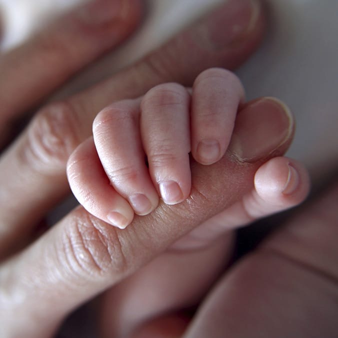 Gros plan sur la main d'un bébé attrapant le doigt de sa maman.