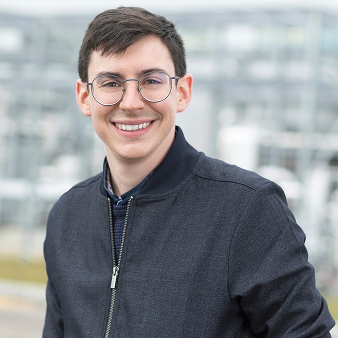 A dark-haired young man with glasses smiles.