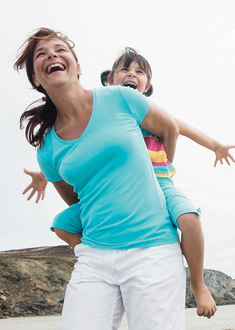 A woman carrying a little girl on her back. Both people smile.